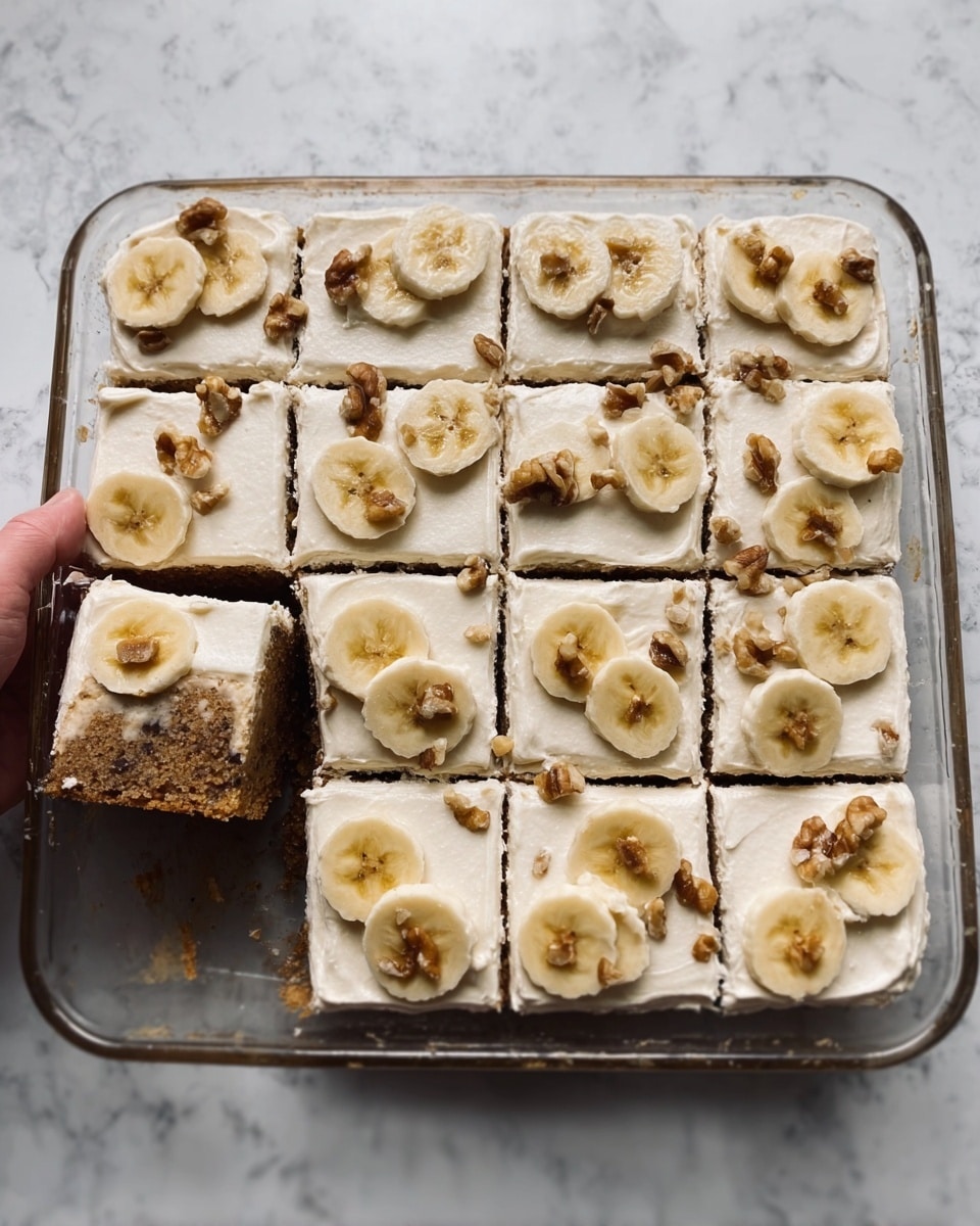 The image shows a rectangular glass baking dish filled with a cake cut into 20 square pieces. The cake has two main layers: a darker brown bottom layer resembling a moist cake or bread, and a thick top layer of creamy white frosting. Each piece is decorated with a thin banana slice and small walnut pieces scattered on the frosting. One piece has been removed from the dish near the center, showing the texture of the cake inside. A woman's hand is holding one of the cut pieces near the dish. The dish is placed on a white marbled surface. Photo taken with an iphone --ar 4:5 --v 7