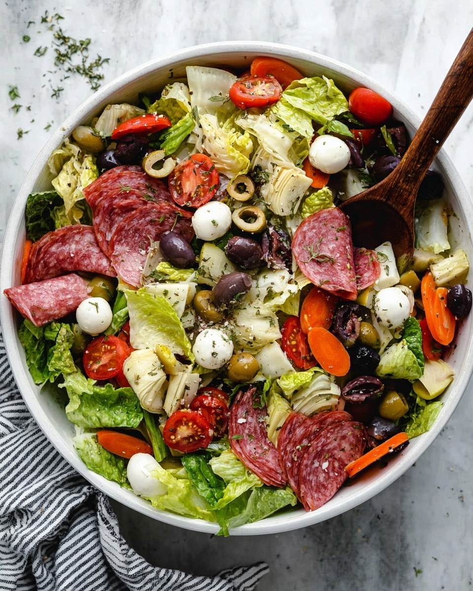 A large white bowl filled with a mixed salad containing several layers: the base is bright green lettuce leaves, layered with thin slices of pink and white salami, small white mozzarella balls, and cubed pale yellow cheese. Scattered through the salad are sliced green and black olives, sliced orange carrots, triangular pieces of pale artichoke hearts, and halved red cherry tomatoes. The salad is sprinkled with dried herbs, and there is a dark wooden spoon partially inside the bowl resting on the salad. The bowl is placed on a white marbled texture surface with a small striped cloth nearby. Photo taken with an iphone --ar 4:5 --v 7