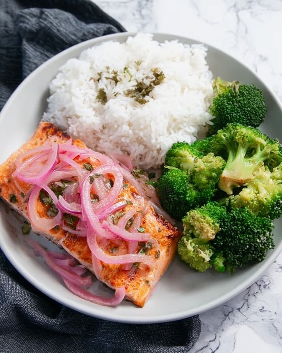 A white plate shows a meal with three parts: a triangular piece of cooked salmon topped with thin slices of pink onion and small green herbs on the left side, a heap of white rice with a soft, fluffy texture placed at the top center, and bright green broccoli florets with a slightly rough surface on the right side. The plate sits on a white marbled surface with a dark cloth partially visible underneath. photo taken with an iphone --ar 4:5 --v 7