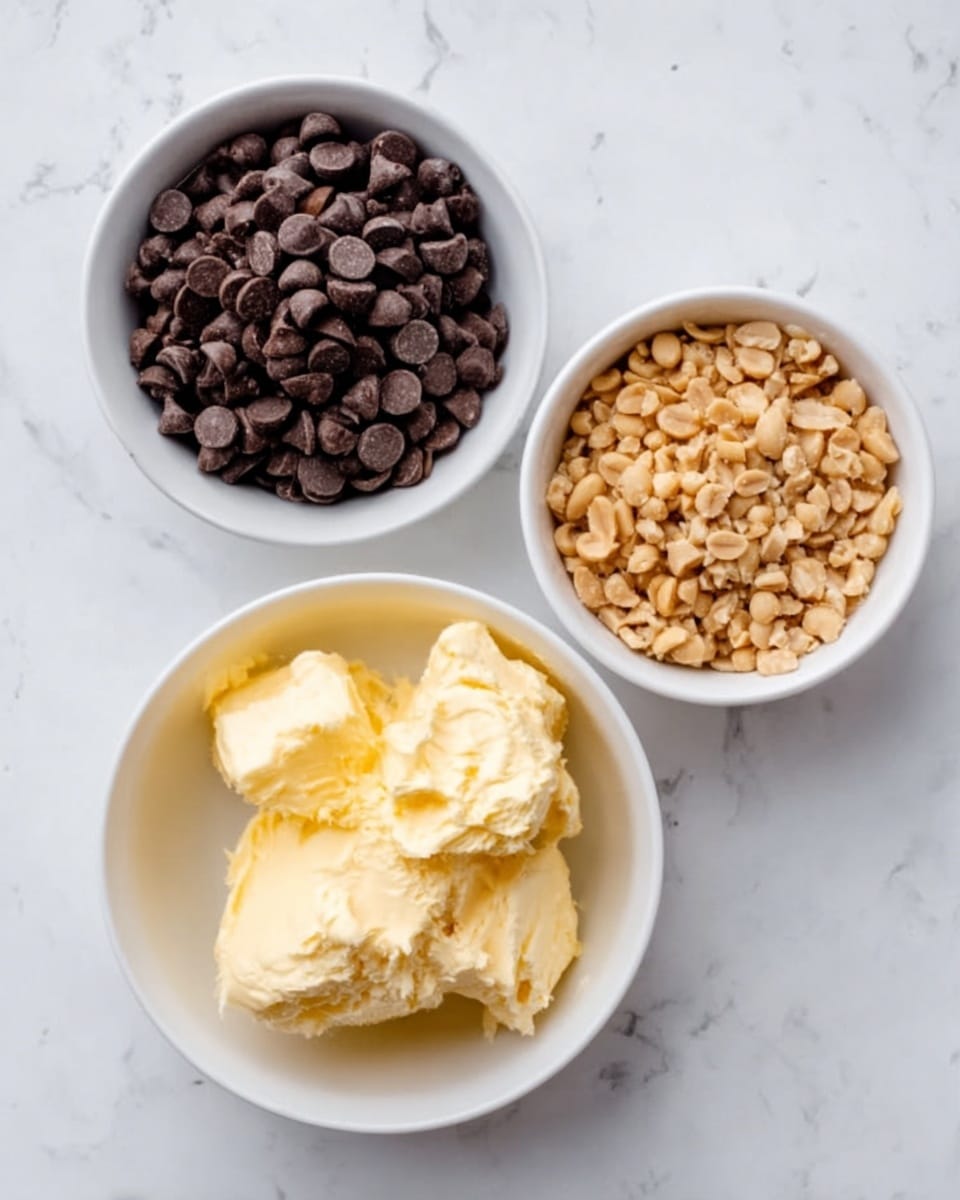 The image shows three white bowls placed on a white marbled surface. The top left bowl is filled with dark brown chocolate chips, smooth and shiny. The top right bowl contains light brown crushed peanuts with a rough texture. The bottom larger bowl holds soft, creamy yellow butter or margarine with a slightly uneven texture from being scooped. The bowls are arranged in a triangular shape. photo taken with an iphone --ar 4:5 --v 7
