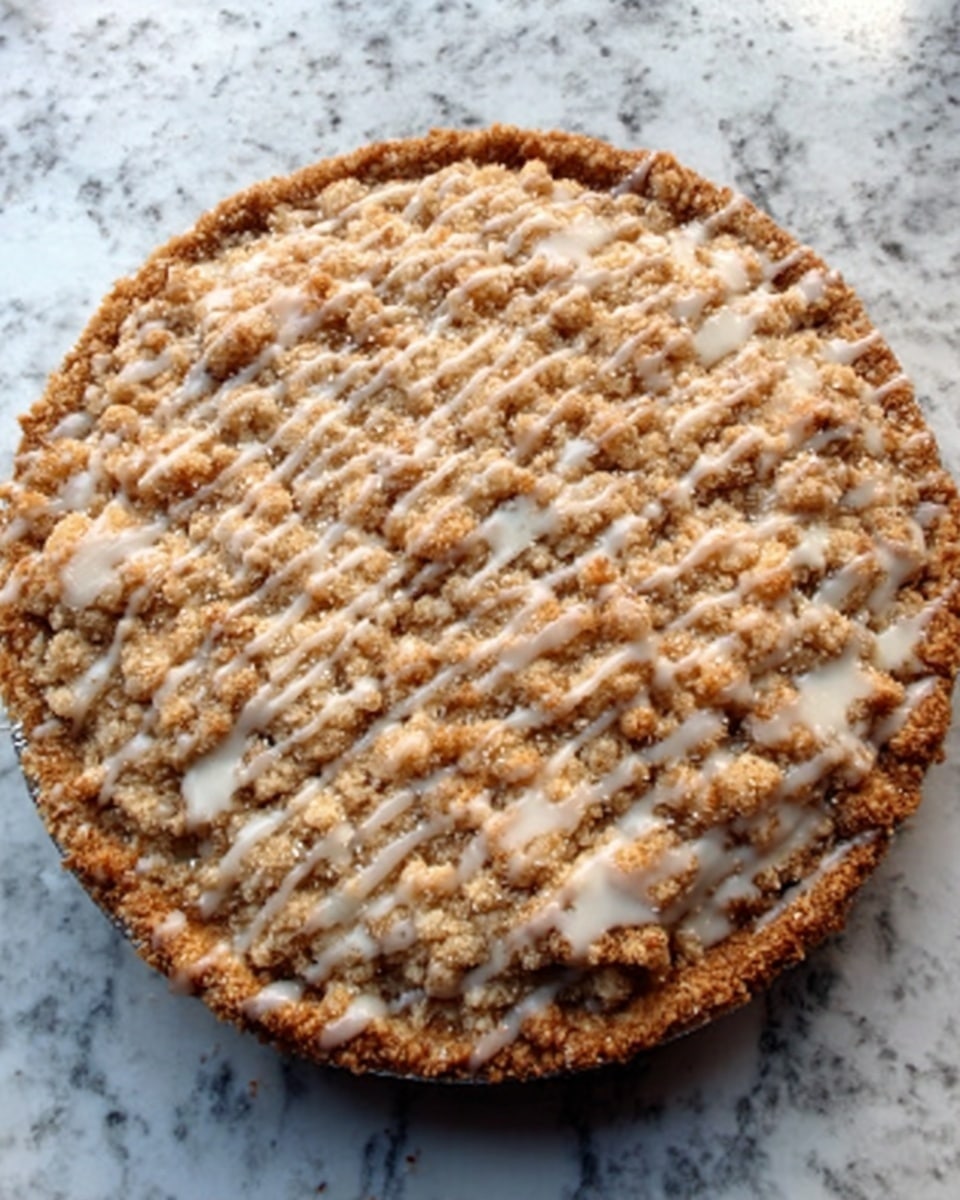 A round pie with a thick crumbly top layer that looks golden brown and rough in texture, sprinkled unevenly with white icing drizzle in small patches. The pie sits on a white marbled surface. The crust edges are visible around the sides, slightly darker and firm. photo taken with an iphone --ar 4:5 --v 7