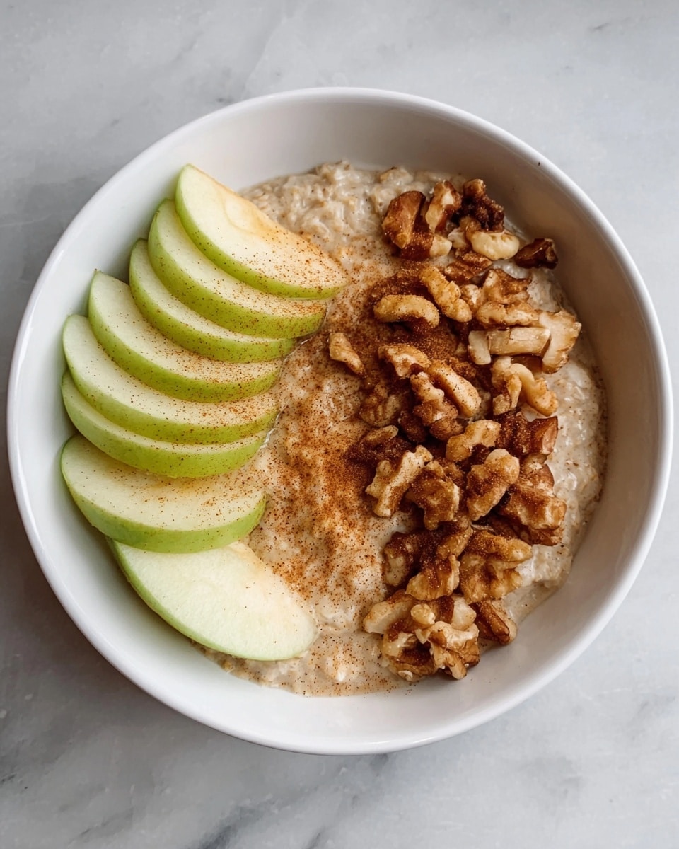 A white bowl holds a layered dish with three main parts. On the left, there are thin slices of green apple, slightly overlapping in a neat row. In the middle, there is a creamy beige oatmeal base with a smooth texture. On the right, a pile of chopped walnuts adds a rough, crunchy look. The oatmeal has a bit of brown cinnamon sprinkled lightly on top, blending with the oats. The bowl sits on a white marbled surface. Photo taken with an iphone --ar 4:5 --v 7
