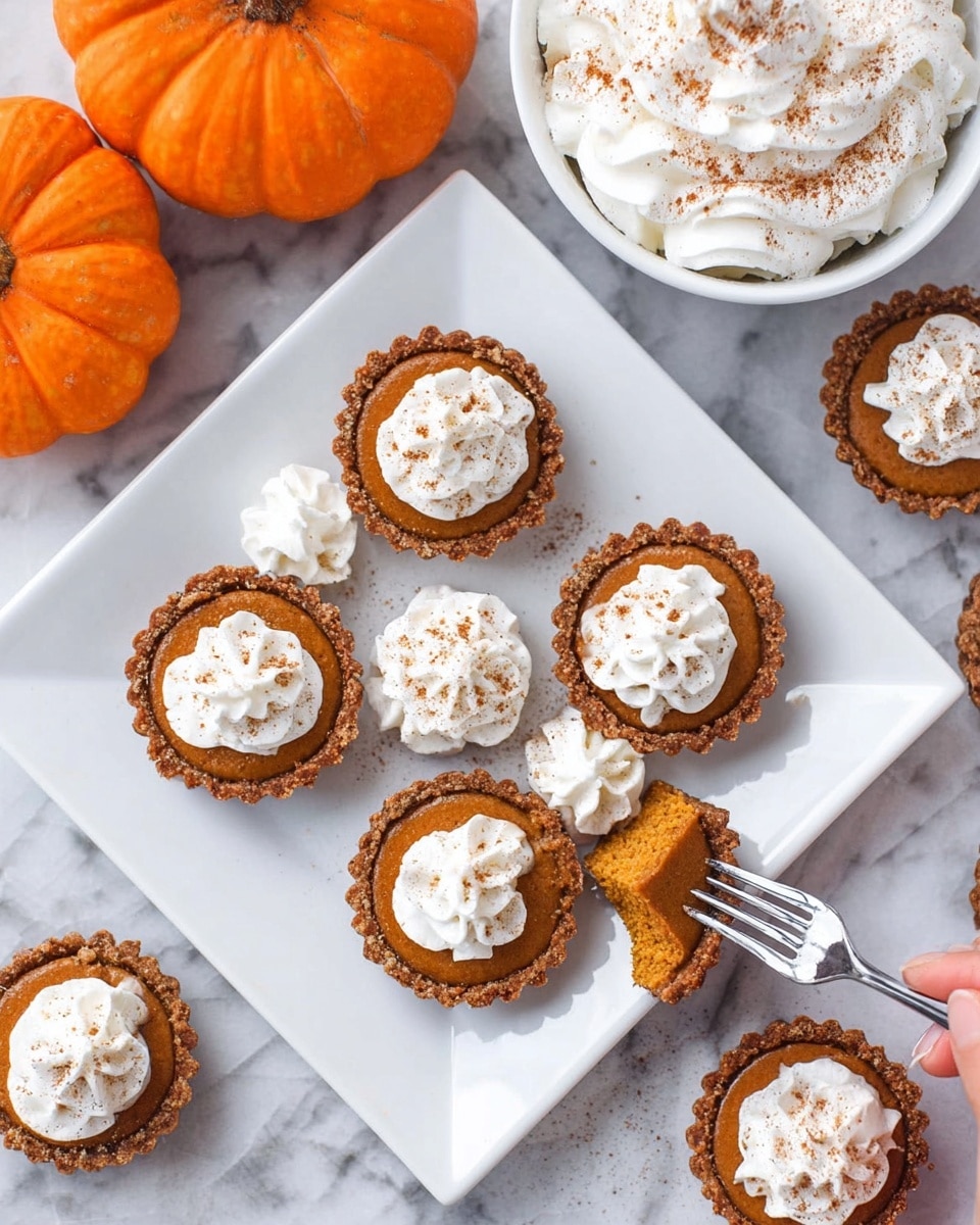 The image shows small pumpkin tarts arranged on a white square plate and white marbled surface. Each tart has a brown crust and a smooth orange pumpkin filling topped with a swirl of white whipped cream sprinkled lightly with cinnamon. One tart is cut in half, revealing the soft filling inside, with a woman's hand holding a fork next to it. Small dollops of whipped cream are placed around the plate for decoration. In the background, there is a bowl filled with whipped cream sprinkled with cinnamon and two small orange pumpkins adding a festive touch. Photo taken with an iphone --ar 4:5 --v 7