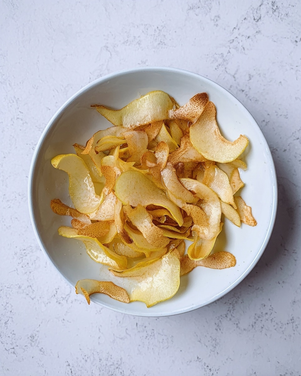 A white bowl with thin, uneven pear peels inside, showing a mix of light yellow and brown colors. The peels lie in a loose pile, some pieces curling slightly, with a shiny, wet texture from a light drizzle of liquid. The bowl is set on a white marbled surface, giving a clean and simple look. photo taken with an iphone --ar 4:5 --v 7