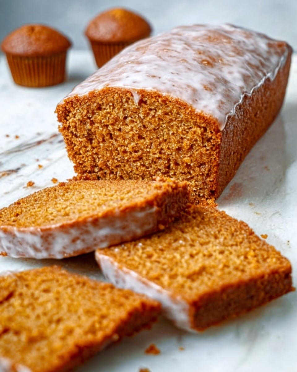 The image shows a loaf of glazed pumpkin bread placed on a white marbled surface. The bread has a shiny, light icing glaze on top, visible as a smooth, slightly cracked layer that covers the entire loaf. Several thick slices are neatly arranged in front of the loaf, showing the dense, moist, orange-brown texture inside. In the background, there are three small muffins with a similar brownish color, slightly blurred to keep focus on the bread. The lighting is soft and natural, highlighting the texture and glaze. photo taken with an iphone --ar 4:5 --v 7