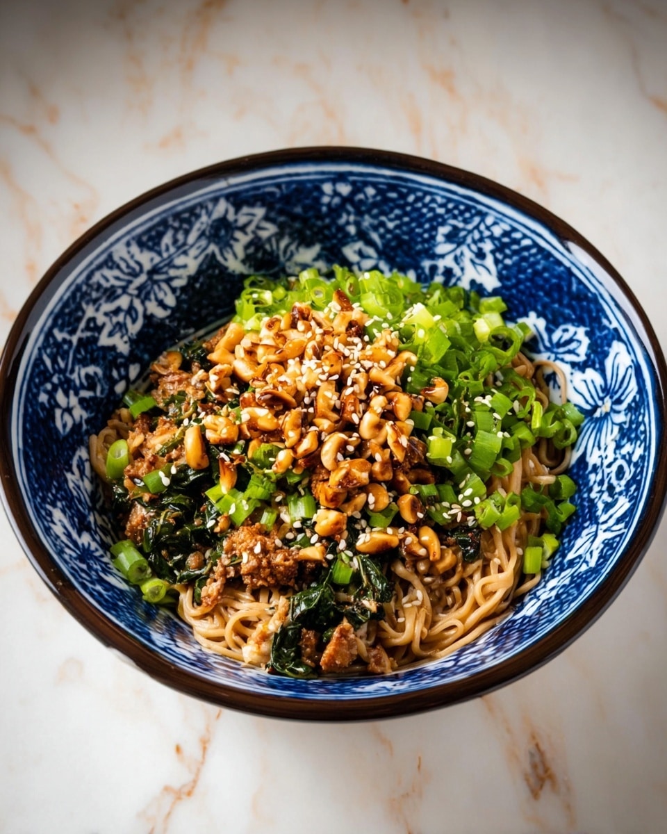A white bowl with blue and white floral patterns is filled with three layers of food. The bottom layer is light brown cooked noodles mixed with bits of dark green leafy vegetables and small pieces of cooked meat. On top of the noodles, there is a layer of chopped green onions that add a bright green color. The top layer is golden brown roasted nuts scattered all over, mixed with white sesame seeds sprinkled across the dish. The bowl is placed on a white marbled surface. photo taken with an iphone --ar 4:5 --v 7