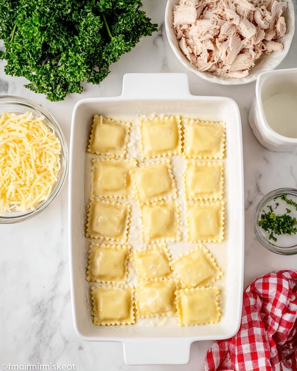 The image shows a white rectangular baking dish filled with one layer of square ravioli pieces, each having a light yellow color and a crimped edge, placed over a thin layer of creamy white sauce. Above the dish, there is a white bowl filled with shredded pale pink cooked chicken. To the left, a glass bowl contains shredded pale yellow cheese. To the right of the chicken, a bunch of fresh curly parsley adds a bright green touch to the scene. The surface under everything is white with a marbled pattern, and a small part of a white cup and a red and white checkered cloth are visible on the bottom right corner. Photo taken with an iphone --ar 4:5 --v 7