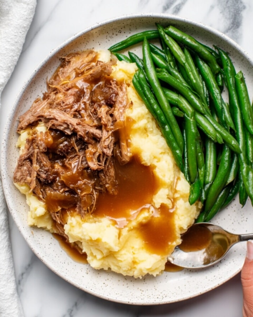 The image shows a white bowl filled with creamy pale yellow mashed potatoes at the base. On top, there is a thick layer of dark brown shredded meat in gravy, slightly glossy and textured with strands and chunks. To the right side of the meat, bright green peas are stacked, looking fresh and firm. A silver spoon rests in the bowl, with a woman's hand visible holding the edge. The bowl sits on a white marbled surface. Photo taken with an iphone --ar 4:5 --v 7