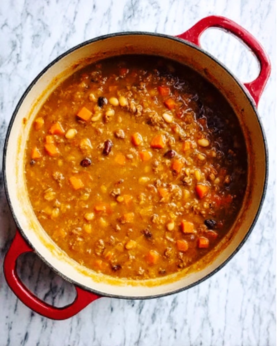 A white pot with red handles filled with thick stew. The stew has a rich yellowish-brown color with visible beans, small chunks of orange carrots, and pieces of meat throughout. The texture looks hearty and chunky, with the stew almost reaching the top edge of the pot. The pot is placed on a white marbled surface. Photo taken with an iphone --ar 4:5 --v 7