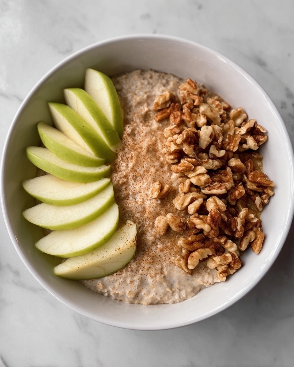 The image shows a white bowl with three main layers. On the left side, there are thin, light green slices of apple arranged in a neat fan shape. In the middle, there is a light brown, creamy oatmeal layer with a smooth texture. On the right side, there is a pile of chopped walnuts with a crunchy look, showing different shades of brown. The bowl is placed on a white marbled surface. Photo taken with an iphone --ar 4:5 --v 7