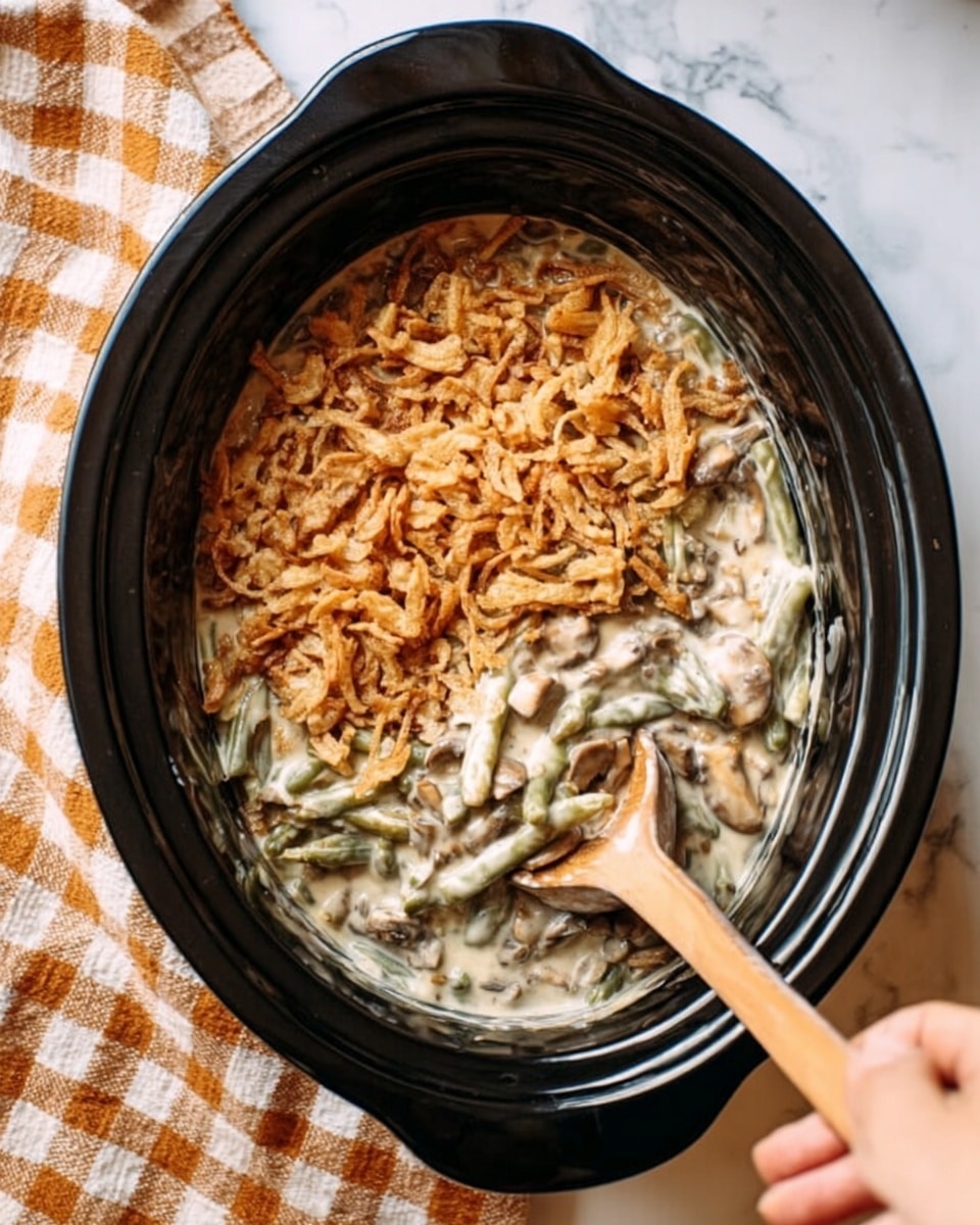 The image shows a black slow cooker filled with a creamy green bean casserole. The bottom layer is green beans covered in a thick, creamy white sauce with visible mushroom pieces. The top layer is a golden-brown crispy fried onion topping spread evenly over the casserole. A wooden spoon is stirring the casserole from the bottom right side, held by a woman's hand. The slow cooker is sitting on a white marbled surface with a beige and orange checkered cloth beside it. photo taken with an iphone --ar 4:5 --v 7