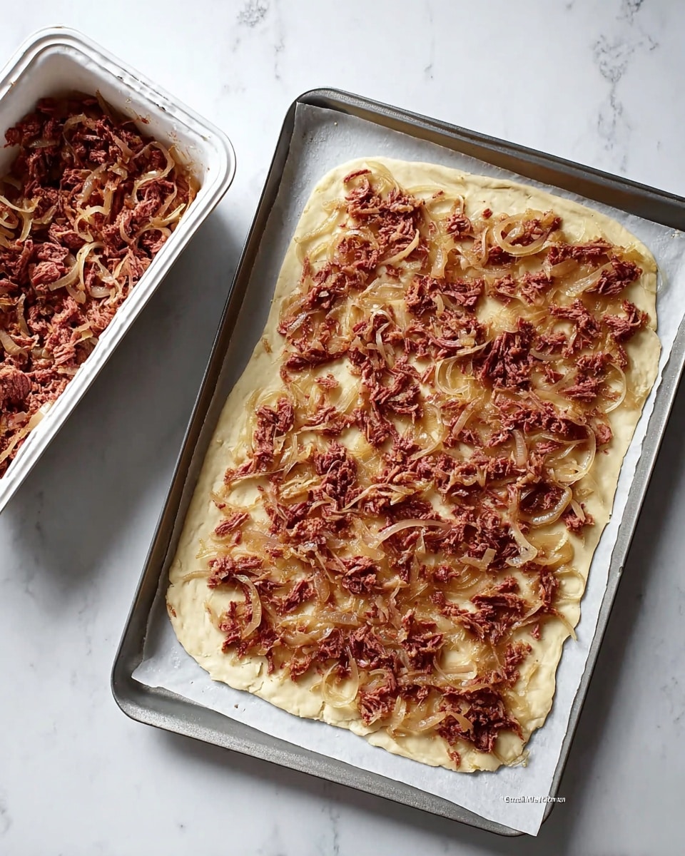 A rectangular piece of thin dough is laid flat on a baking tray lined with white parchment paper, topped with a spread of shredded reddish meat mixed with translucent cooked onion slices. To the top left of the baking tray, there is a white aluminum container filled with more of the same shredded meat and onions. The scene is set on a white marbled surface. photo taken with an iphone --ar 4:5 --v 7