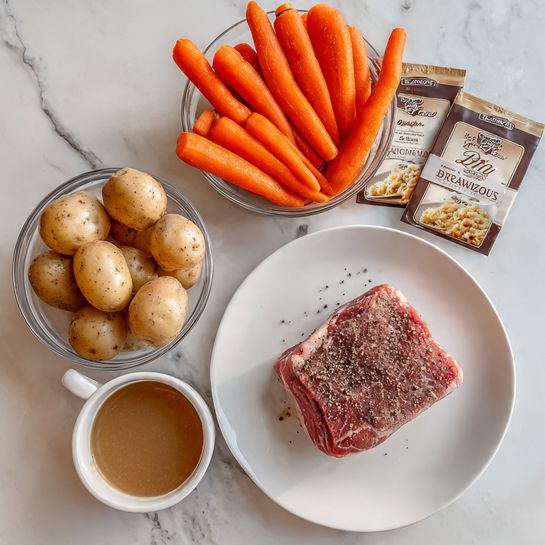 The image shows a white plate holding one piece of raw beef seasoned with coarse black pepper, positioned slightly to the right of the frame. Above the plate, there is a white bowl filled with bright orange baby carrots, and to the left of that, a clear glass bowl with small, light brown potatoes. Below the potatoes is a small white bowl filled with smooth brown gravy, with two packets placed beside it; one is a white Lipton Recipe Secrets packet and the other is a McCormick Brown Gravy packet with an image of mashed potatoes and meat. The items rest on a white marbled surface. Photo taken with an iphone --ar 4:5 --v 7