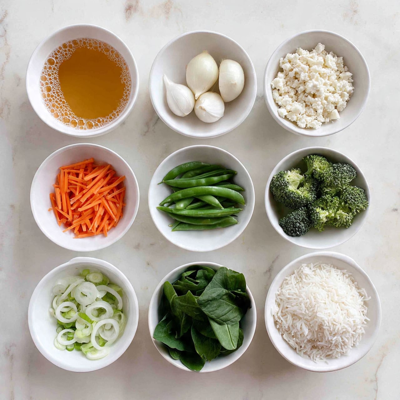The image shows nine white bowls with different ingredients arranged on a white marbled surface. Starting from the top left, a bowl contains a light orange liquid with bubbles on top. Next to it on the right is a bowl full of small white crumbly pieces. Below the liquid bowl is a bowl with three whole peeled small white onions, and next to it is a bowl filled with thinly sliced orange carrot sticks. Below the carrot is a bowl containing bright green snap peas, and to the right is a bowl with small green broccoli florets. Underneath the broccoli is a bowl with sliced white rings of green onions, and to the left is a bowl filled with small chopped white onions. At the very bottom is a bowl containing fresh dark green spinach leaves, and on the right beside it is a bowl with fluffy white rice. The photo taken with an iphone --ar 4:5 --v 7