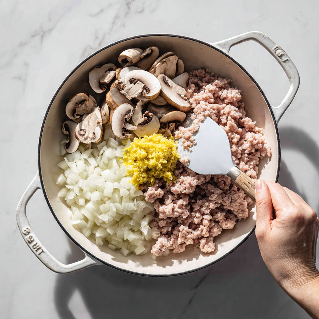 A black frying pan on a white marbled surface holds several layers of ingredients being stirred by a woman's hand with a white spatula. The bottom layer consists of finely chopped white onion spread across most of the pan. On one side, there are thin slices of light brown mushrooms arranged in a small pile. In the center, there is a layer of finely chopped pink meat topped with a small mound of yellow minced garlic or ginger. The pan has a white handle, and the cooking surface is clearly visible. Photo taken with an iphone --ar 4:5 --v 7