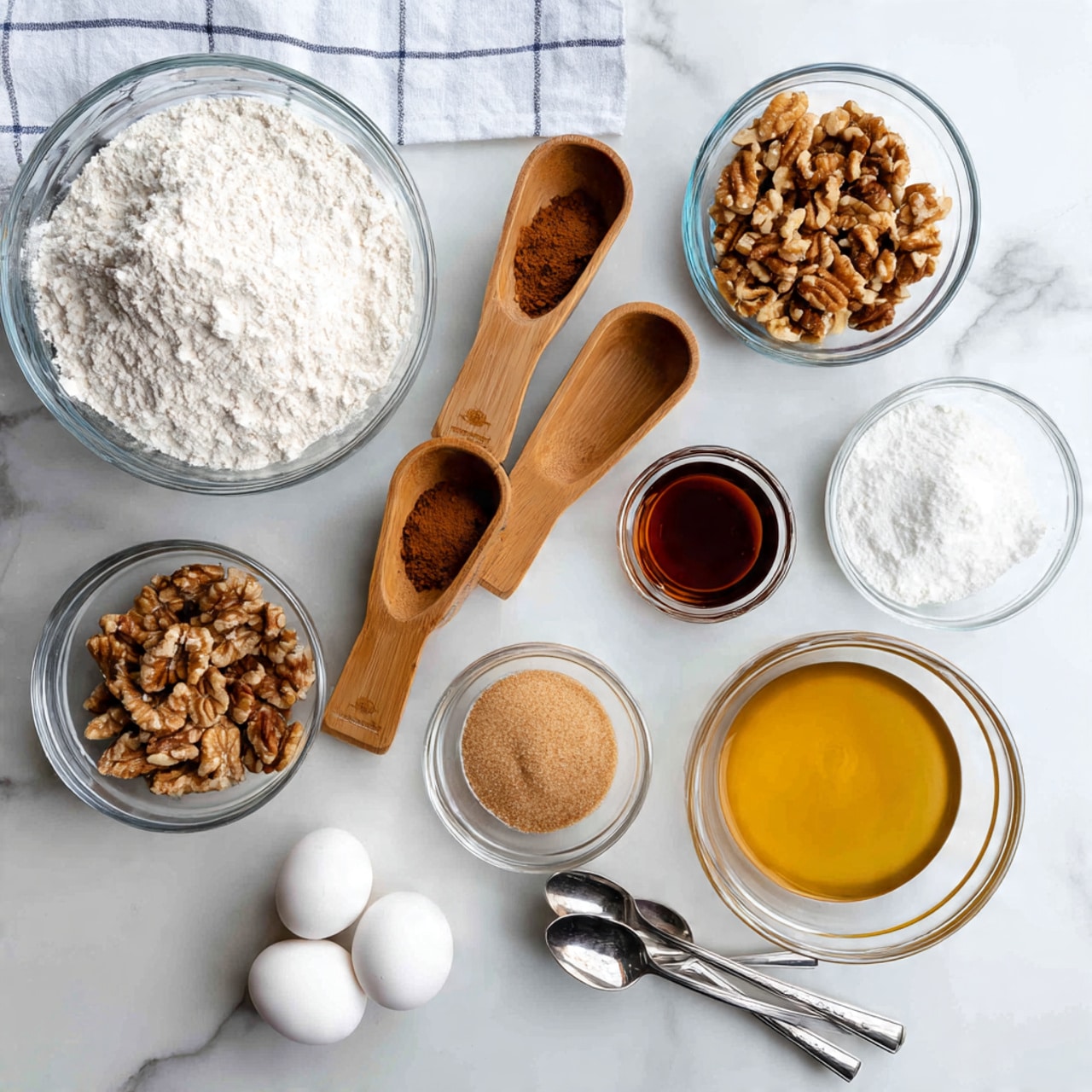 The image shows several clear glass and wooden measuring cups with baking ingredients arranged on a white marbled surface with a white and blue checkered cloth underneath. In the top left, a large clear glass bowl holds white flour with a small pile of brown cinnamon. To its right, another clear bowl contains a white creamy ingredient. Below, two wooden measuring cups rest side by side; one filled with chopped nuts and the other with light brown sugar. To the right of those, a small clear glass cup is filled with a dark brown liquid, likely maple syrup. Below that, a large clear bowl contains melted butter. Next to it, a smaller clear bowl holds two cracked eggs. In the bottom right corner, three silver spoons lay closely together on the white marbled surface. The overall look is bright and clean with a focus on preparing a baking recipe. Photo taken with an iphone --ar 4:5 --v 7