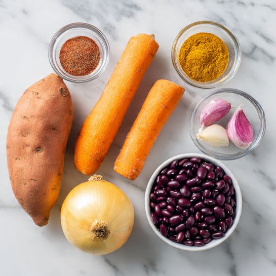 The image shows several ingredients placed on a white marbled surface. There are two orange sweet potatoes on the left, one larger than the other, with a smooth texture. To the right of them is a medium-sized round yellow onion with a dry outer layer. Next is a long, slightly curved bright orange carrot lying horizontally. Above the carrot are three garlic cloves, two pinkish and one white. Near the top, there are two clear glass bowls; the left bowl contains a reddish-brown spice powder and the right bowl has a lighter yellow-brown spice powder. On the far right is a white bowl filled with shiny, dark purple-black beans. The arrangement is neat and spaced out evenly. photo taken with an iphone --ar 4:5 --v 7