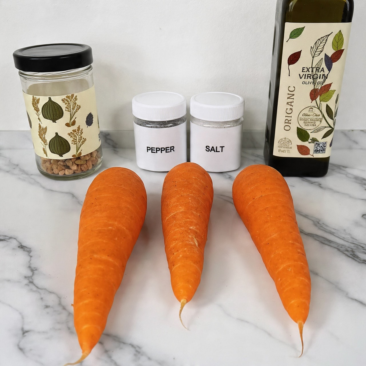 The image shows three thick, bright orange carrots placed side by side on a white marbled surface. Behind them, there are two small white jars with white lids labeled