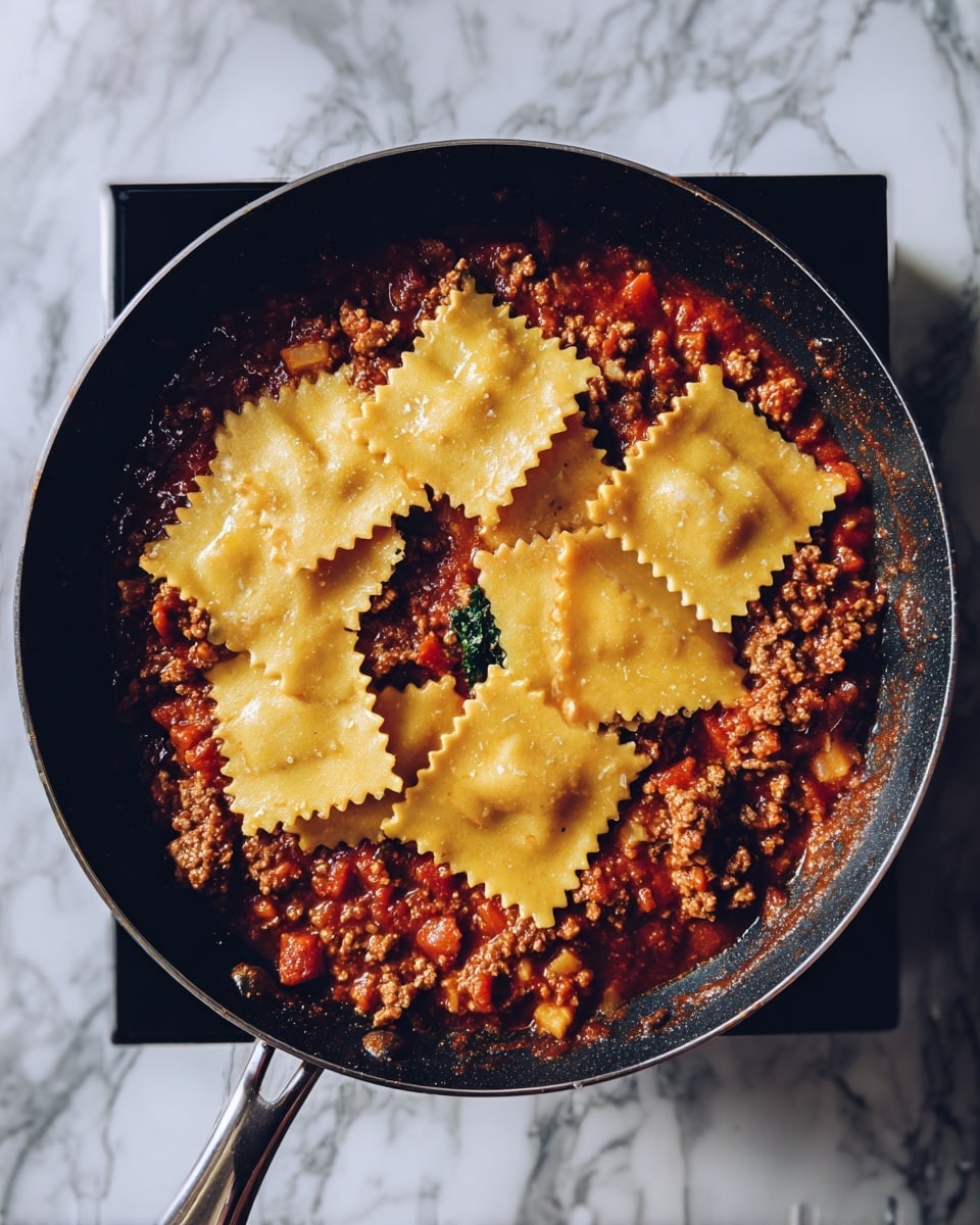 A black pan sits on a stove with a mix of chunky brown and red sauce with small pieces of meat and diced vegetables visible at the bottom. On top of the sauce, there are soft yellow dry lasagna sheets placed irregularly, some slightly overlapping and some standing upright around the edges. The background has a white marbled surface. Photo taken with an iphone --ar 4:5 --v 7