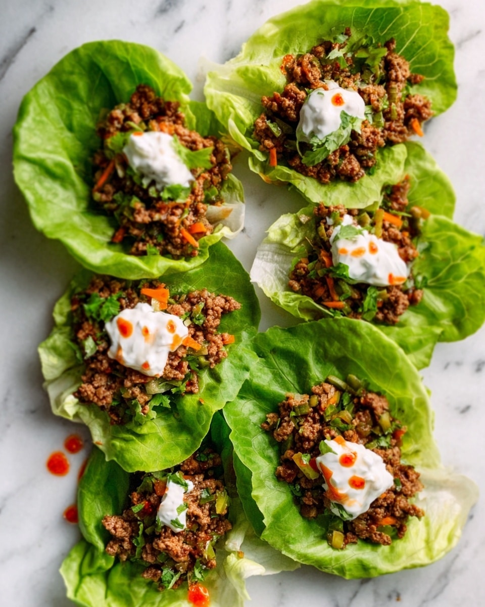Five fresh, bright green lettuce leaves lie on a white marbled surface, each topped with a layer of cooked ground meat mixed with small pieces of vegetables in earthy tones. On top of the meat in the center of each lettuce wrap is a small dollop of creamy white sauce. The texture of the lettuce looks crisp and fresh, contrasting with the crumbly, slightly textured meat layer underneath. There are small spots of reddish-orange sauce scattered gently over the wraps. Photo taken with an iphone --ar 4:5 --v 7