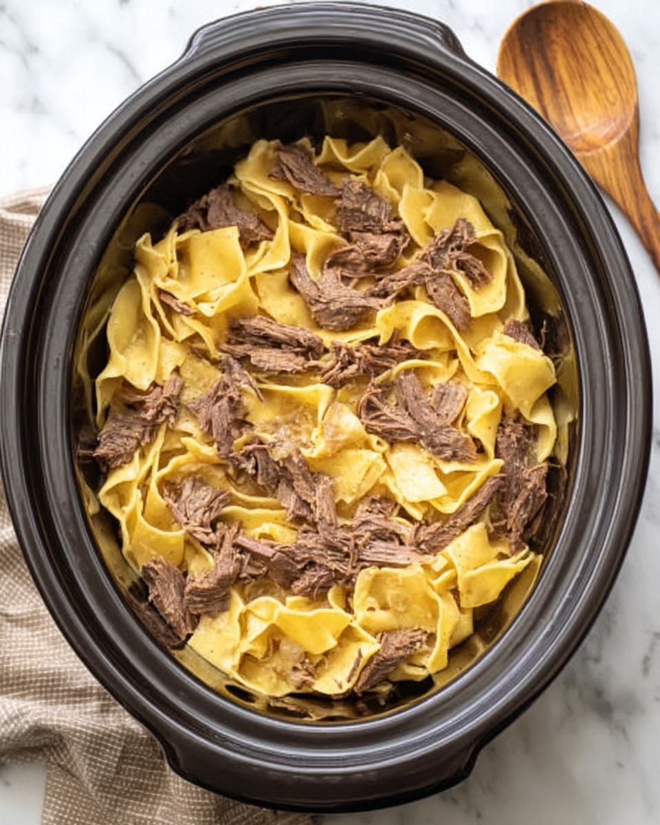 The image shows a black slow cooker filled with wide, flat yellow noodles layered with pieces of brown cooked meat, all mixed together inside. The noodles have a soft, slightly wrinkled texture, and the meat looks tender and thinly sliced, spread evenly throughout the dish. The slow cooker is placed on a white marbled surface with a wooden spoon next to it. The overall look is warm and hearty. photo taken with an iphone --ar 4:5 --v 7