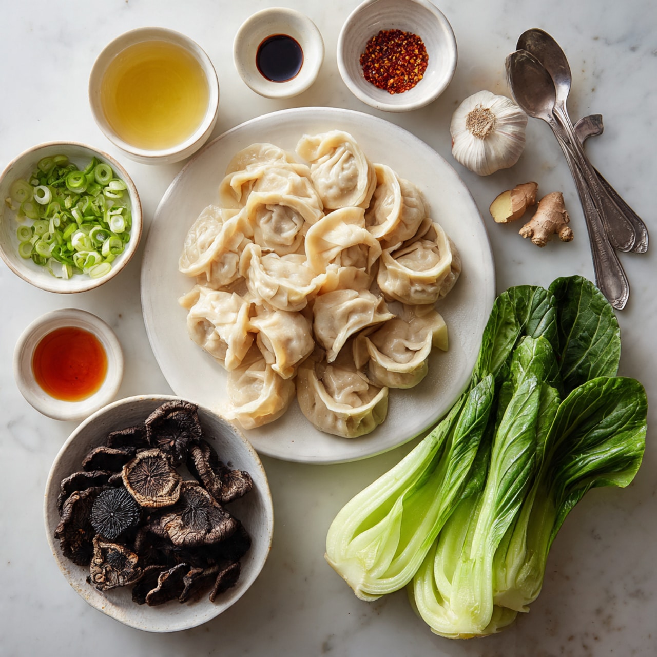 The image shows a white plate filled with a pile of uncooked dumplings that have a pale beige and slightly translucent dough, with soft folds and a slightly ridged texture on top. To the right of the dumplings, there are three fresh bok choy leaves with bright green, crinkled tops and thick, white stems, dotted with water drops. Below the dumplings, a white bowl holds several dark brown, wrinkled dried mushrooms with varied shapes and textures. Above the dumplings, a small white bowl is filled with chopped green onions, showing bright green and pale white rings. Around the main items, there are several small white bowls and spoons containing various ingredients: a small bowl with dark soy sauce, a bowl with light yellow liquid, a bowl with a reddish-brown sauce, a spoon with black pepper, and a plate with peeled ginger root and several garlic cloves. All items sit atop a clean white marbled surface. photo taken with an iphone --ar 4:5 --v 7