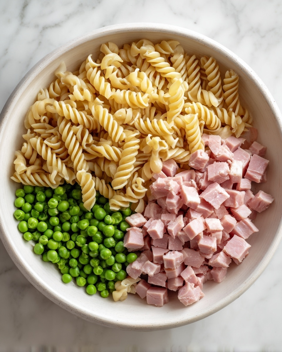 A round white wooden bowl sits on a white marble surface, filled with three separate sections of ingredients. One section has dry spiral pasta with a pale yellow color and smooth texture. Another section holds small, bright green peas with a slightly shiny surface. The last section contains small cubes of pink ham, showing a soft and slightly moist texture. No ingredients overlap, and the arrangement creates a clear, colorful contrast. Photo taken with an iphone --ar 4:5 --v 7