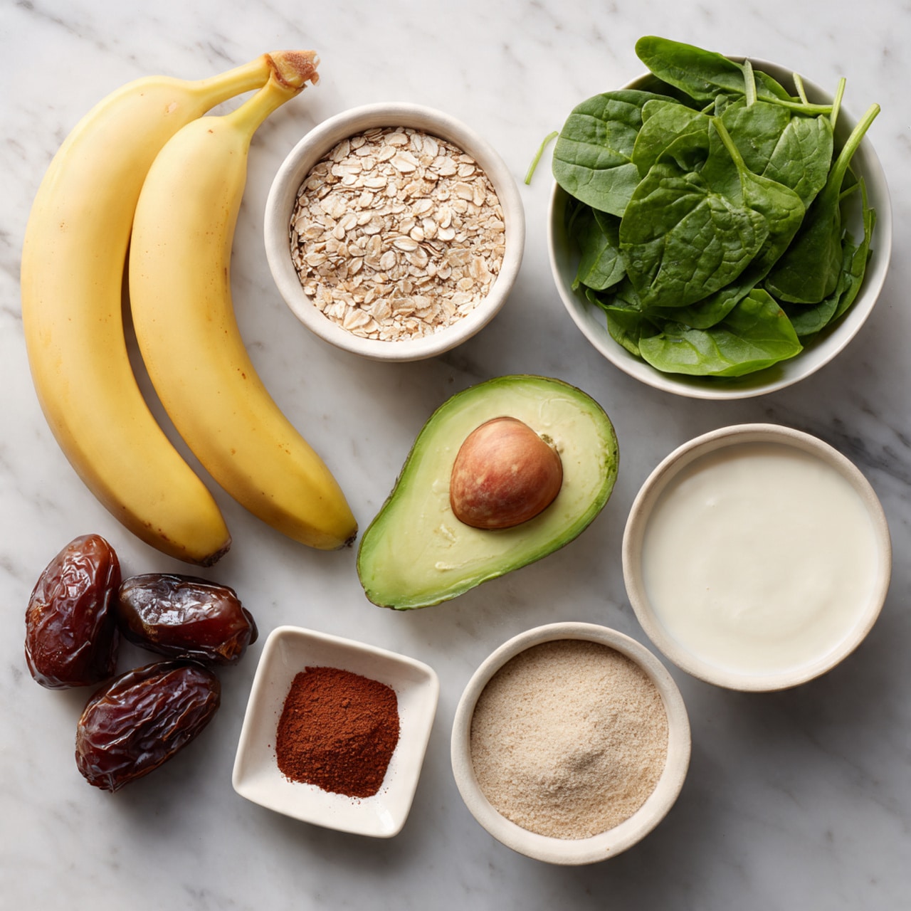 The image shows a white marbled surface with several ingredients neatly placed. There are two ripe yellow bananas on the left side. Above them, there are two small white bowls filled with light brown and beige seeds. To the right of these bowls, there is a white bowl filled with fresh green spinach leaves. Below the spinach, there is a half avocado with the seed removed, showing its light green inside. Next to the avocado, there are two dark brown dates. Below the bananas, a small white square bowl holds a reddish-brown powder, and next to it, a round white bowl contains a fine beige powder. On the far right, a larger white bowl is filled almost full with a white creamy liquid. Finally, at the bottom right, another white bowl holds coarse white salt. The arrangement is clean, colorful, and evenly spaced. Photo taken with an iphone --ar 4:5 --v 7