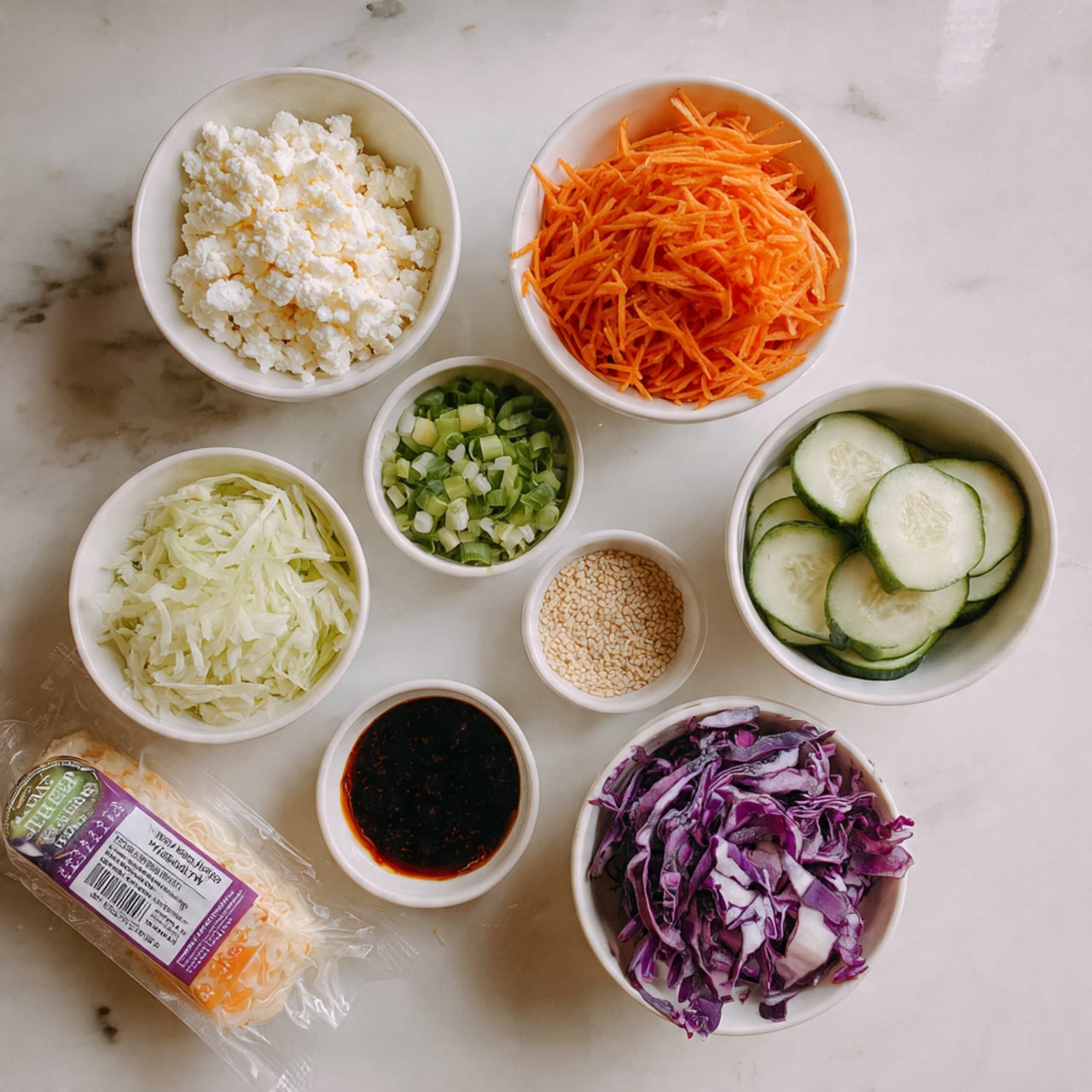 A top-down view of an arrangement of small white bowls and a packaged item on a white marbled surface. Starting from the upper left, there is a white bowl filled with crumbled white cheese. To the right, a white bowl holds thinly shredded orange carrots. Below the cheese, another white bowl contains finely chopped green onions. In the center, a small white bowl is filled with light brown sesame seeds. To the right, a white bowl holds thin, round slices of cucumber. Below the carrots, there is a white bowl filled with thin strips of purple cabbage. At the bottom left is a white bowl containing a dark soy sauce. Next to the bowls on the left is a sealed package of pre-shredded carrots with a label. The bowls are arranged neatly on the marbled white surface, creating a clean and colorful presentation. Photo taken with an iphone --ar 4:5 --v 7