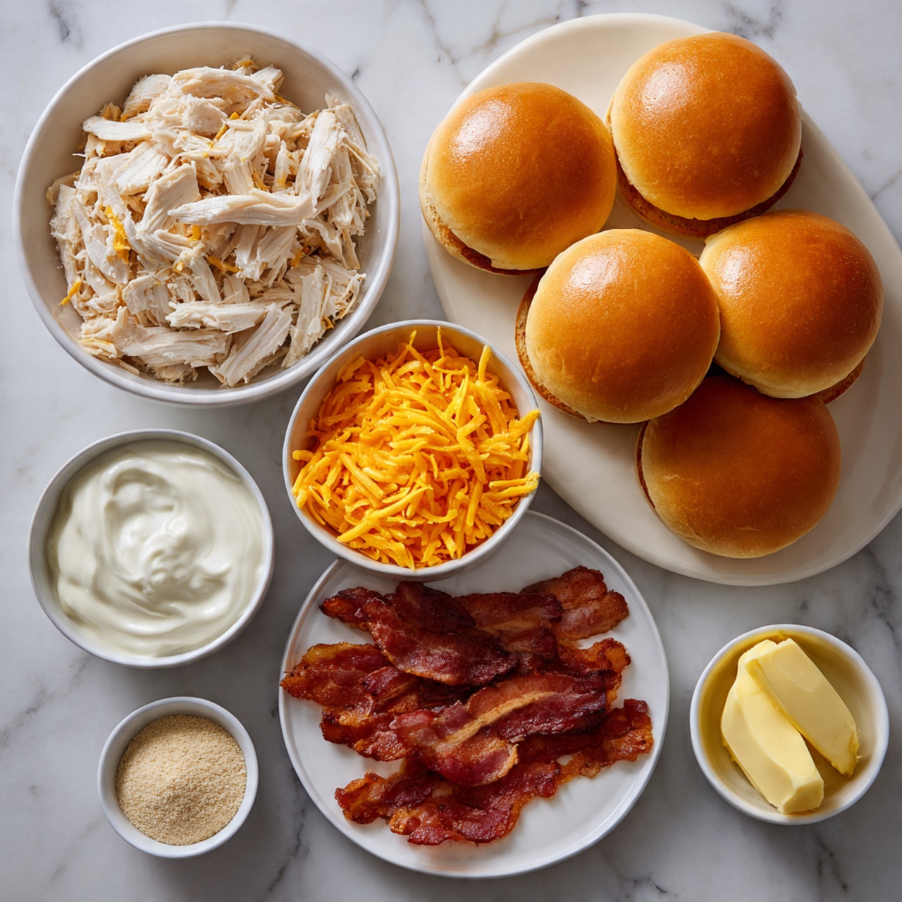 A display of sandwich ingredients arranged neatly on a white marbled surface includes eight soft golden brown sandwich buns in two rows of four stacked together at the top right; below them on a white plate are several crispy, cooked bacon strips with a rich reddish-brown color. To the left side is a large white bowl filled with shredded white cooked chicken, showing varying chunky textures. Above it is a medium white bowl full of bright orange shredded cheese strands. Nearby is another white bowl holding a smooth white sauce or dressing. To the right bottom are two small white dishes: one containing a light beige powder, likely seasoning, and the other holding a softened yellow spread, possibly butter or mayonnaise. Photo taken with an iphone --ar 4:5 --v 7