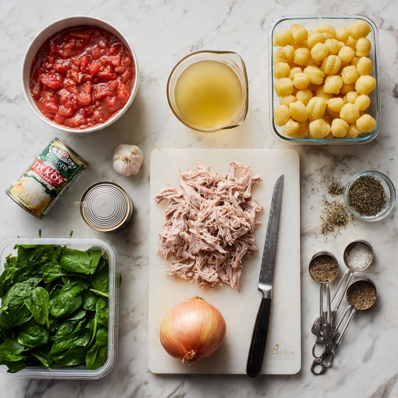 The image shows cooking ingredients laid out on a white marbled surface, including a white bowl filled with shredded pink meat in the top right, a clear plastic container of yellow gnocchi pieces to its left, and a glass measuring cup of yellow broth near the top center. Below these, there is a can of red diced tomatoes open on the left side, a whole garlic bulb and some garlic cloves scattered nearby, and a plastic container filled with fresh green spinach leaves on the bottom left. Towards the middle, a white cutting board holds finely chopped white onions next to a whole peeled onion, with a large knife resting on the board to the right. There is a small open jar of fennel seeds and two metal measuring spoons filled with dried herbs scattered near the bottom right. The overall scene looks clean, organized, and ready for cooking, photo taken with an iphone --ar 4:5 --v 7