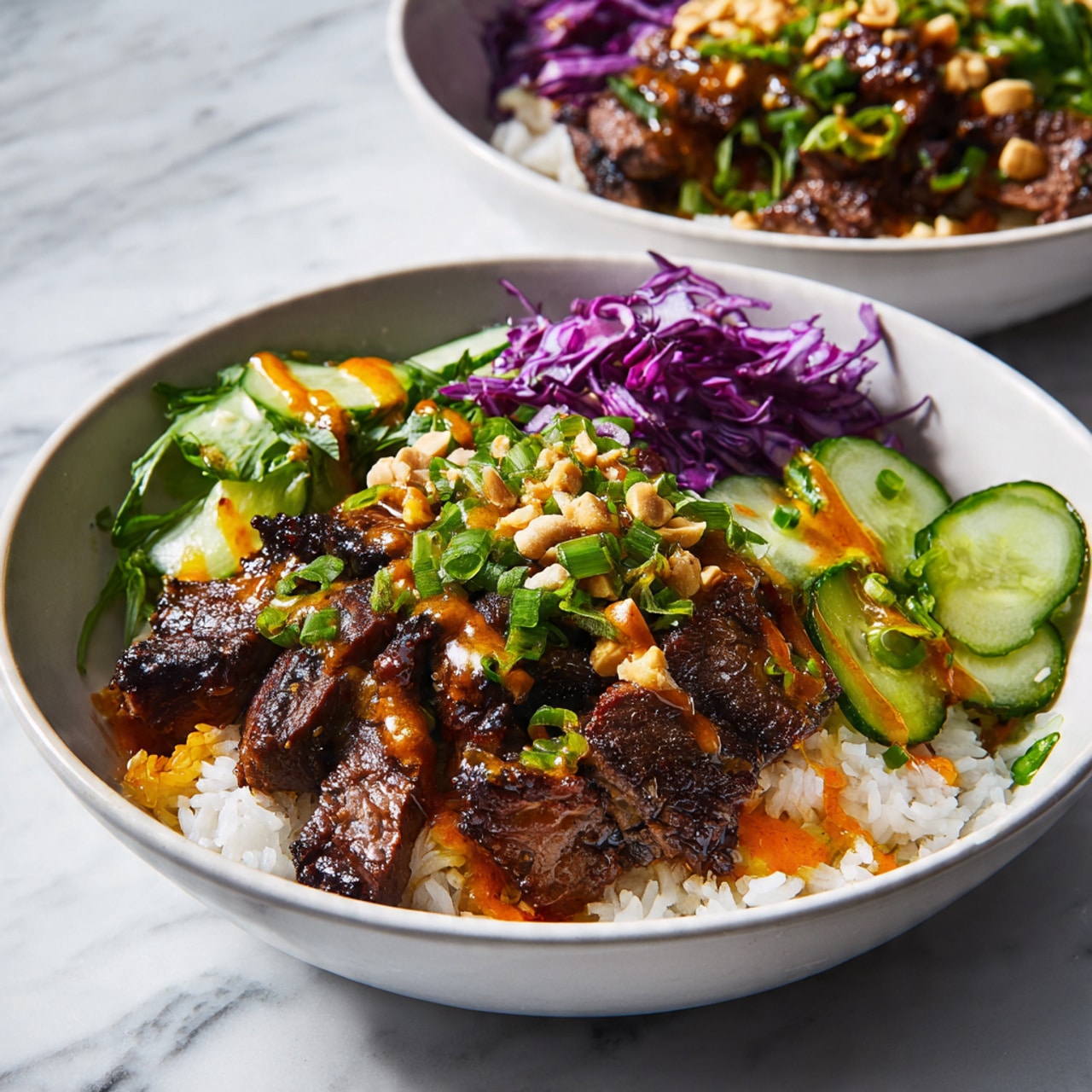 The image shows a white bowl filled with a base layer of white rice. On top of the rice, there is a generous amount of grilled meat with a dark brown, slightly shiny glaze. Around the meat, there are fresh cucumber slices on one side and thin shredded purple cabbage on the other side. Bright green chopped spring onions and crushed peanuts are sprinkled over the meat. An orange sauce is drizzled in thin lines over the top. Behind the bowl, there is another similar bowl blurred out on a white marbled surface. photo taken with an iphone --ar 4:5 --v 7