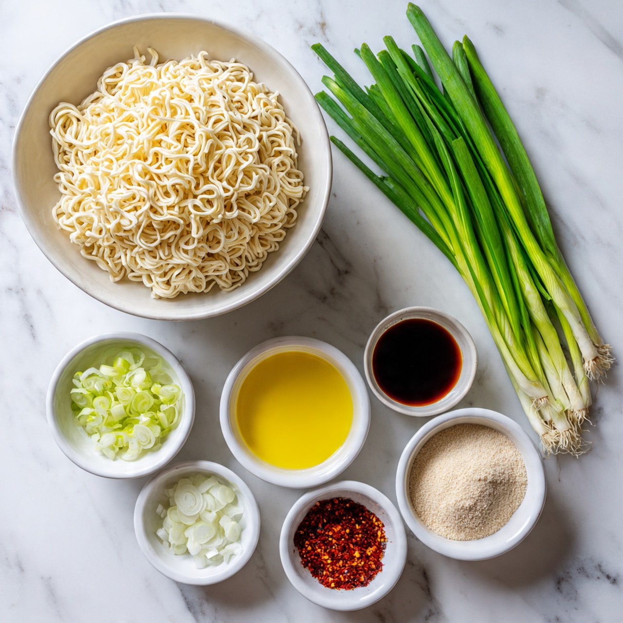The image shows a white bowl filled with uncooked ramen noodles, placed at the top left. To the right of the bowl are several fresh, green spring onions standing upright. Below the noodles and spring onions, five small white bowls are arranged neatly: the left one contains chopped white onion, next to it is a bowl with bright yellow oil, followed by a bowl with dark brown soy sauce, then a small bowl with red chili flakes, and finally a bowl with light beige powder. All items are set on a white marbled surface. Photo taken with an iphone --ar 4:5 --v 7