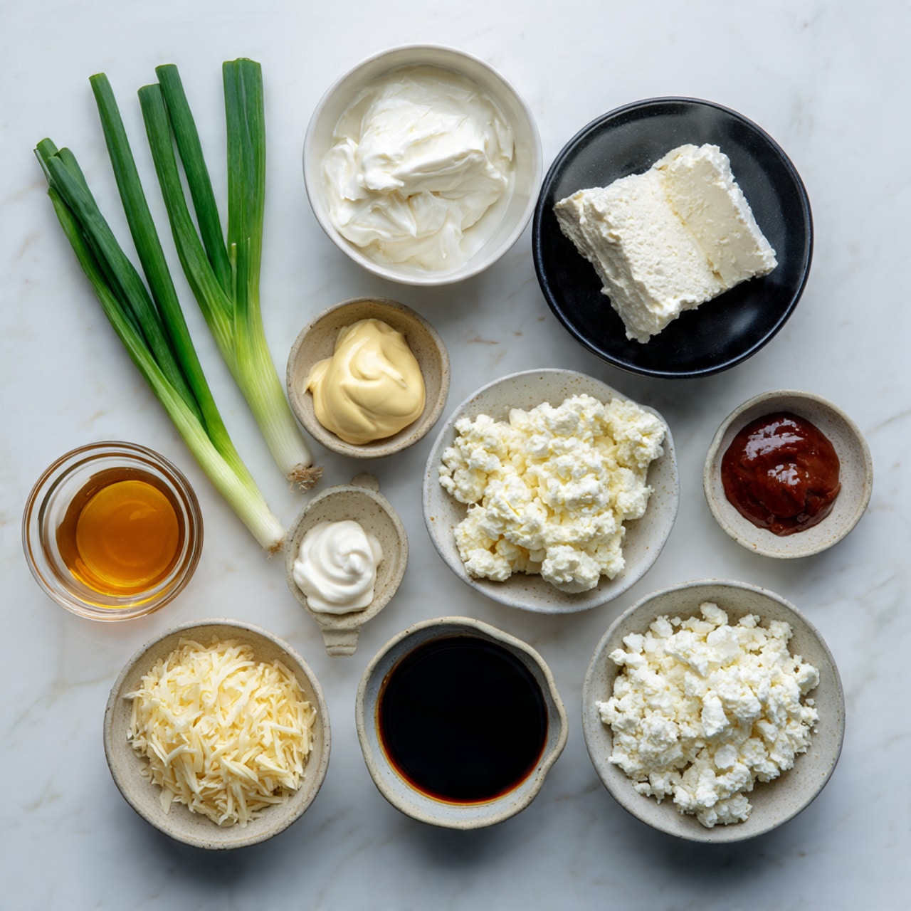 The image shows a flat lay of eleven small bowls and three green onions on a white marbled surface. From top left, there are three long green onions. Below the onions, there is a small white bowl with a soft white cream cheese. To the right, a black bowl holds a dollop of soft white cream cheese. Next to it, a white bowl contains a moist block of white cheese. Below this, a white bowl of dark soy sauce is on the right side. A small glass bowl with golden honey is placed beside it. On the bottom left, a light gray bowl is filled with pale yellow shredded cheese. Near it, a small black bowl contains a thick light yellow mayonnaise dollop. At the center, a light gray bowl is filled with crumbly white cheese. To the right bottom, a white bowl holds reddish-brown chili sauce. Another black bowl with dark soy sauce is near the bottom center. The bowls are neatly arranged with clean edges, and the white marbled surface adds a smooth, clean look. Photo taken with an iphone --ar 4:5 --v 7