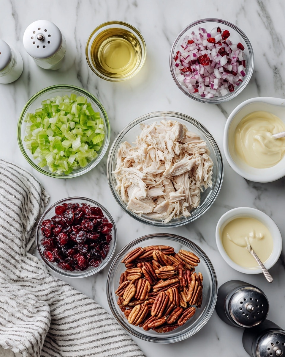 The image shows a white marble surface with several small clear glass bowls arranged neatly. Each bowl contains a different ingredient: shredded cooked chicken, light green chopped celery, dark red dried cranberries, chopped red onions, whole pecans, and three small bowls with salt, mayonnaise, and a pale yellow liquid, likely juice or oil. White salt and black pepper grinders stand nearby, and a white and grey striped cloth napkin lies on the corner of the surface. The setup is clean and organized, viewed from above. Photo taken with an iphone --ar 4:5 --v 7