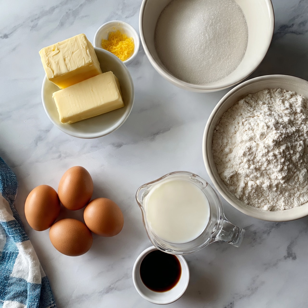 square image The image shows ingredients for baking arranged neatly on a white marble surface. There are two blocks of pale yellow butter on a small white bowl in the top left with a small bowl of yellow zest nearby. To the right, a large white bowl contains white sugar, with another large bowl of white flour below it. In the bottom left, three brown eggs rest directly on the marble, while beside them a clear measuring cup holds creamy white milk. Below the milk is a small white bowl filled with dark vanilla extract. A blue and white checkered cloth is partially visible on the left side. Photo taken with an iphone --ar 4:5 --v 7