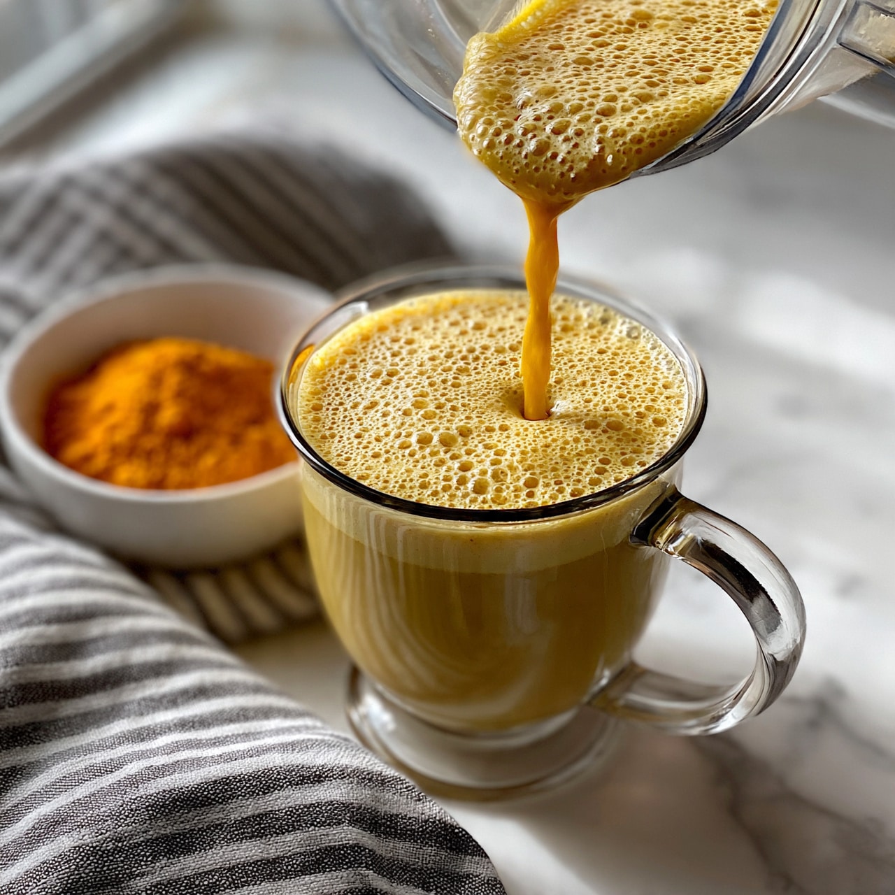 square image A white bowl filled with a smooth, bright yellow turmeric drink topped lightly with black pepper flakes. The bowl sits on a white marbled surface with scattered turmeric roots and a small white bowl holding a dark brown spice mix near it. The lighting makes the drink look creamy and warm, with soft shadows around the bowl. The photo taken with an iphone --ar 4:5 --v 7