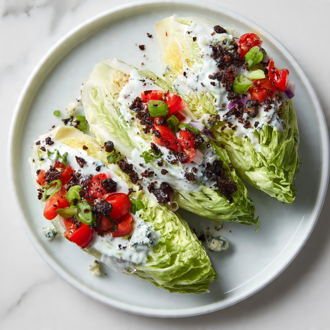 square image A white plate holds three wedge-shaped parts of light green iceberg lettuce, each showing tightly packed, crisp leaves. They are topped with a creamy white dressing and sprinkled with small dark brown crumbles, bright red cherry tomato pieces, green chopped scallions, and bits of purple onion. Scattered blue cheese crumbles add texture and blueish spots. The plate sits on a white marbled surface. photo taken with an iphone --ar 4:5 --v 7