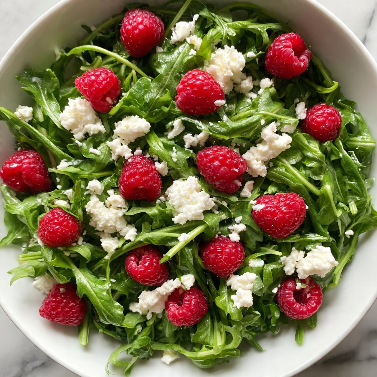 square image A white bowl filled with a salad made of bright green leafy arugula, scattered with fresh, red raspberries, and topped with crumbled white cheese. The salad ingredients look fresh and vibrant, sitting on a white marbled surface. Photo taken with an iphone --ar 4:5 --v 7