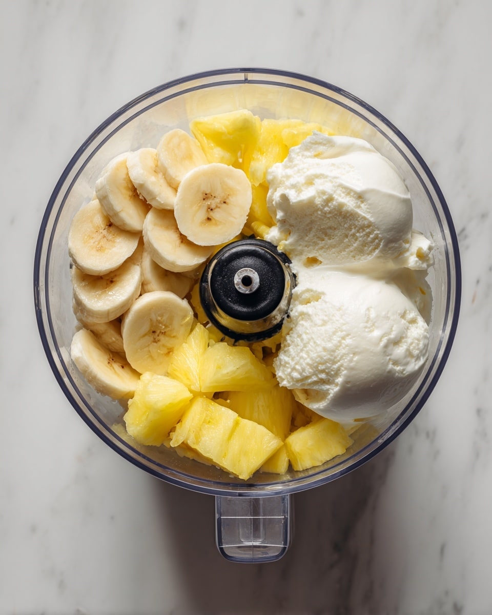 Inside a clear food processor bowl placed on a white marbled surface, there are three main layers of ingredients visible from above: the bottom layer shows bright yellow frozen pineapple chunks, the middle layer has several light yellow banana slices arranged loosely, and the top layer features two large scoops of smooth white coconut cream on one side. The sharp black blade of the processor is partially covered by the ingredients. Photo taken with an iphone --ar 4:5 --v 7
