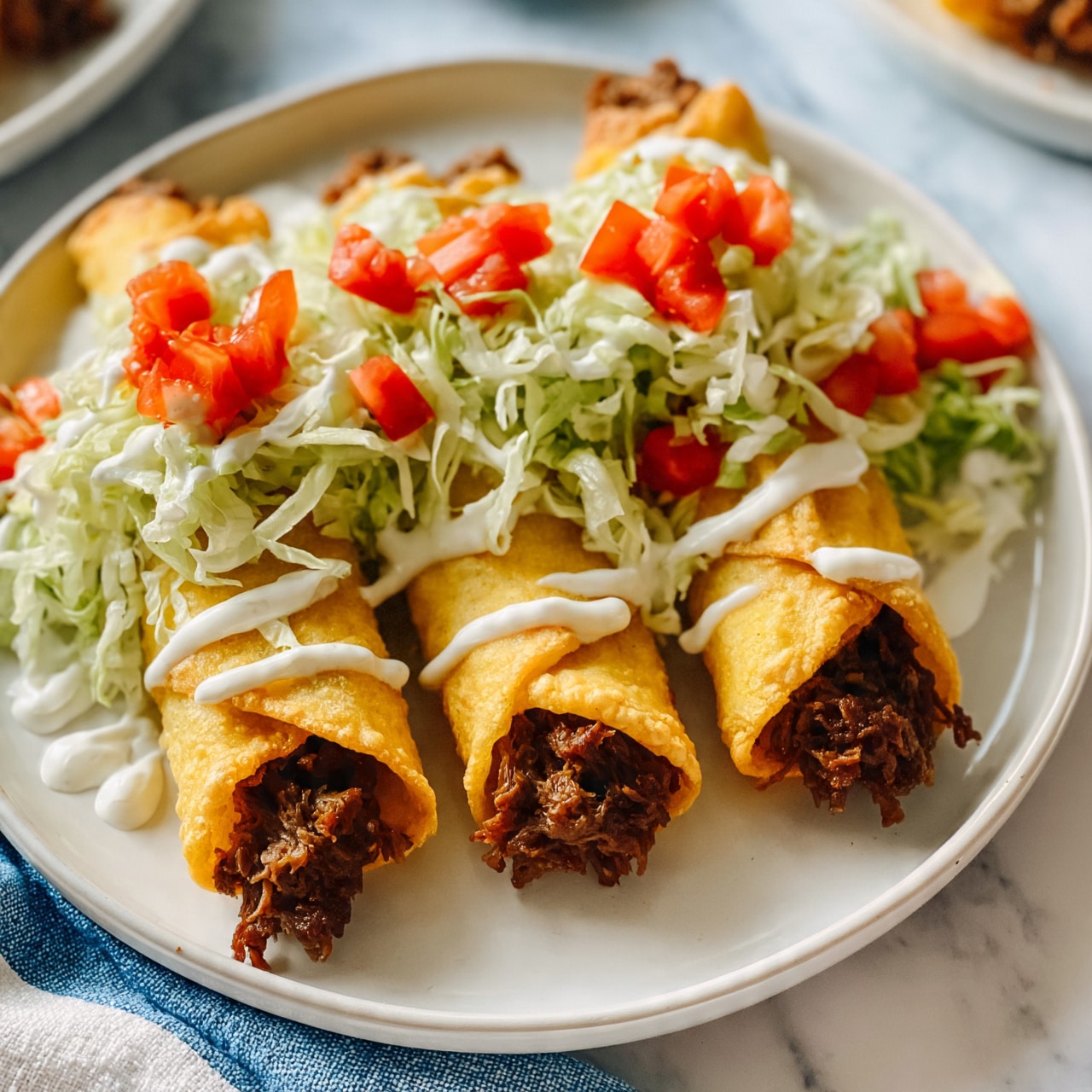 square image The image shows a round white plate on a white marbled surface. The plate holds three rolled crispy golden yellow taquitos filled with dark brown shredded meat, arranged in a row. On top of the taquitos is a layer of finely shredded light green lettuce and small diced red tomatoes scattered over the lettuce. Thin white sauce lines are drizzled over the taquitos and on the lettuce, giving a creamy texture. The blue and white cloth is partially visible under the plate, and parts of other dishes are in the background. Photo taken with an iphone --ar 4:5 --v 7