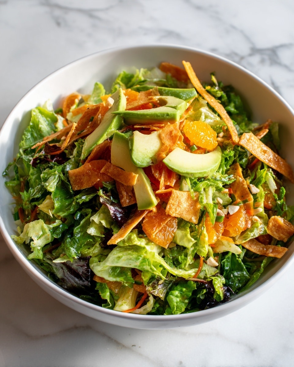 A white bowl filled with a colorful salad on a white marbled surface. The salad has three visible layers: the bottom layer is mixed green leafy lettuce with various shades of light and dark green; the middle layer has small pieces of orange fruit and light tan strips that look like crispy tortilla strips scattered evenly; the top layer includes light green thin slices of avocado and sprinkled small white or cream-colored nuts or seeds adding texture. The colors are bright and fresh, with the green leaves making the orange segments and tan strips stand out clearly. Photo taken with an iphone --ar 4:5 --v 7