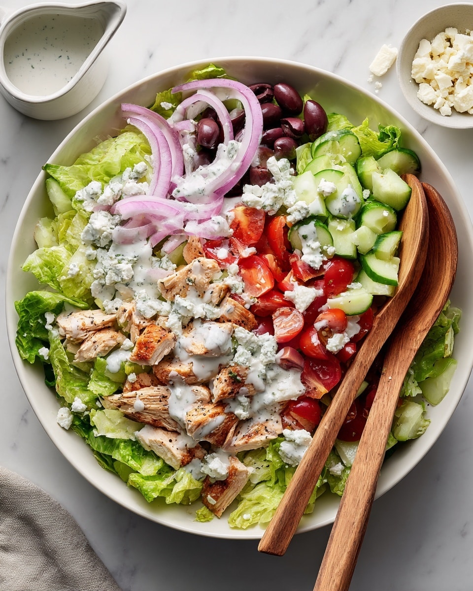 A large white bowl holds a fresh salad with multiple colorful layers. At the bottom is a bed of torn bright green lettuce leaves. On top, there are small pieces of golden-brown roasted chicken scattered evenly, mixed with halved red cherry tomatoes and diced pale green cucumbers. Thin slices of light purple red onion and dark purple Kalamata olives add more color and texture. White creamy dressing is drizzled all over the salad, with small dollops of white cheese crumbles spread on top. Two wooden spoons rest on the edges of the bowl. The bowl sits on a white marbled surface with a small white jug of extra dressing and a small bowl of cheese visible around it. Photo taken with an iphone --ar 4:5 --v 7