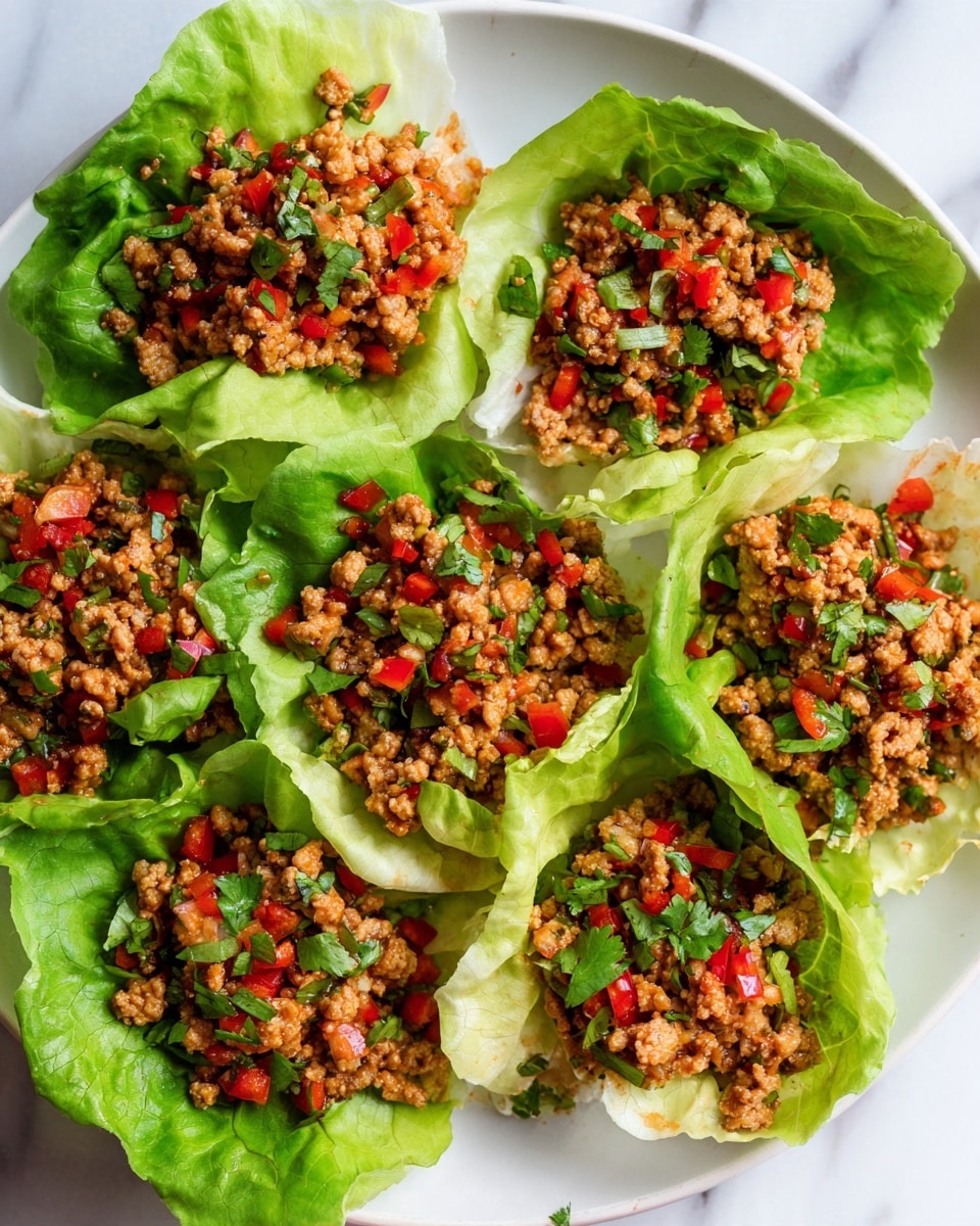 The image shows a white plate filled with six lettuce cups, each holding a layer of minced meat mixed with small pieces of red bell peppers and finely chopped green herbs. The lettuce leaves are fresh and light green, shaping each cup around the filling. The meat filling is crumbly and light brown, spreading evenly inside the crisp lettuce. Tiny diced tomatoes add small red pops throughout the filling, and fresh green herbs are sprinkled on top for a touch of color and texture. The plate sits on a white marbled surface, and a woman's hand is reaching toward the top left corner of the frame. Photo taken with an iphone --ar 4:5 --v 7