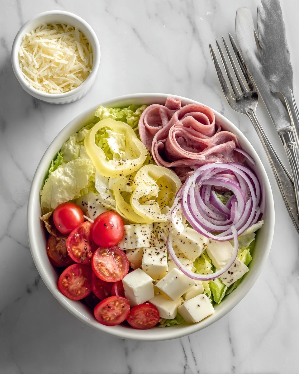 A white bowl holds a fresh salad with several layers and colors: the base is light green and pale yellow romaine lettuce, mixed with thin strips of light pink deli meat and white cheese cubes. Scattered on top are halved bright red cherry tomatoes and thin rings of purple onion. Yellow pepper rings add a pop of color, while a creamy white dressing coats the salad. Black pepper is sprinkled over everything, adding small dark specks. The bowl sits on a white marbled surface next to a white ramekin of grated cheese and two silver forks. Photo taken with an iphone --ar 4:5 --v 7