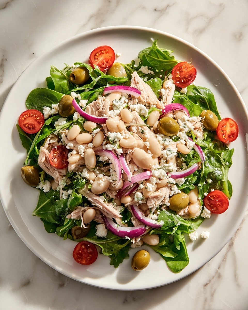 A white plate holds a fresh salad arranged in layers on a white marbled surface. The bottom layer consists of green arugula leaves scattered across the plate. On top are creamy white beans and pale beige chunks of shredded chicken, mixed throughout. Halved cherry tomatoes add bright red pops of color, alongside thin slices of light green olives placed evenly around the plate edge. Thin purple-red onion strips and crumbled white cheese are dotted over the salad. The textures vary from soft beans and chicken to crunchy onions and fresh leafy greens. photo taken with an iphone --ar 4:5 --v 7