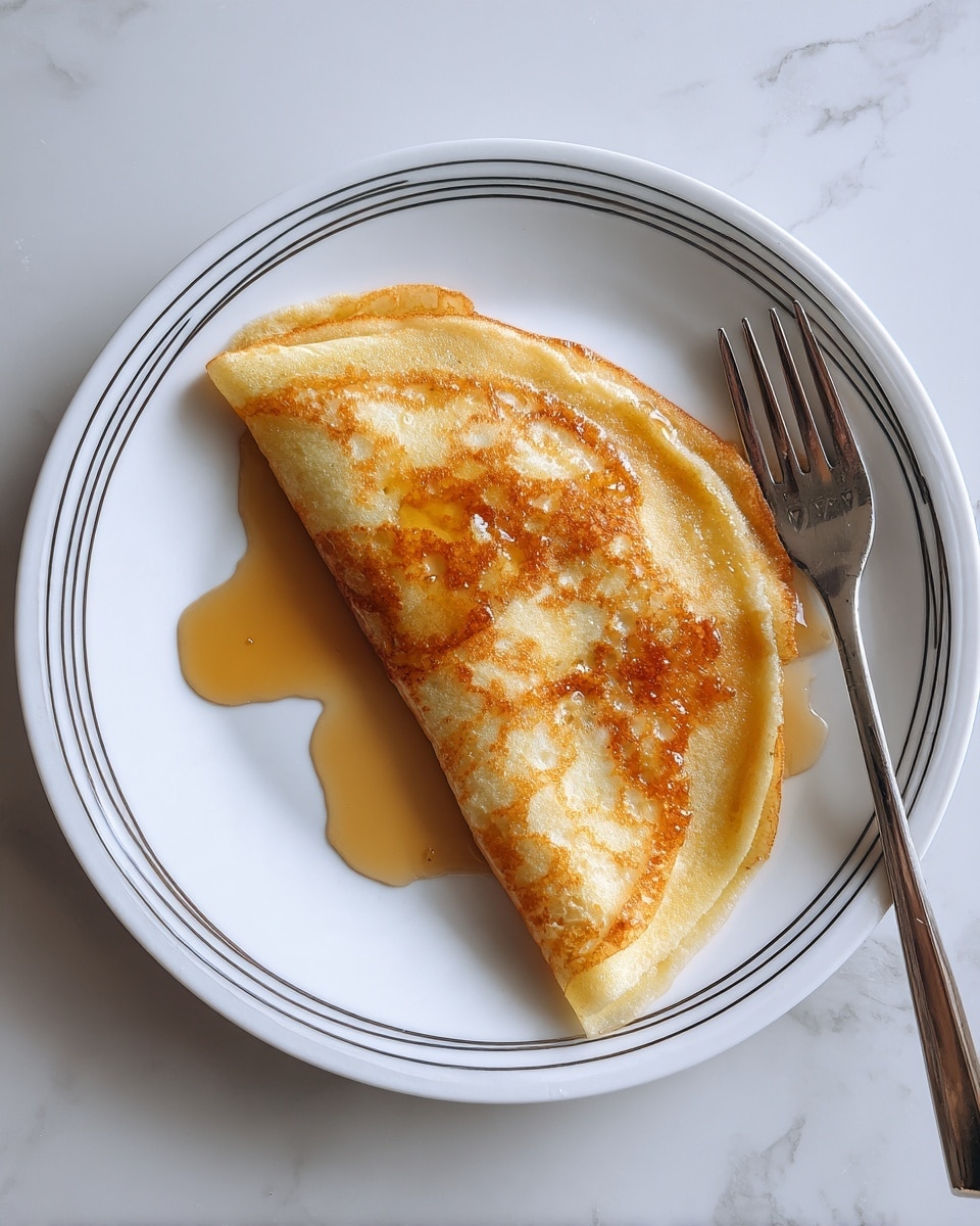 A single folded pancake with a light golden brown color and fluffy texture sits on a white plate with a thin black line design. The pancake is drizzled with light amber syrup that pools slightly on the plate. The plate rests on a white marbled surface. photo taken with an iphone --ar 4:5 --v 7