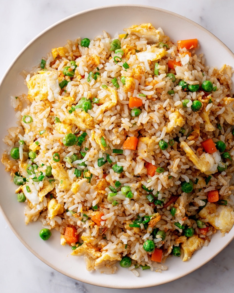 A close-up top view of a round white plate filled with fried rice. The rice is light brown with a slightly oily texture, mixed evenly with small green peas, tiny orange carrot cubes, and bits of scrambled egg, creating a colorful contrast. The plate sits on a white marbled surface, highlighting the warm colors of the dish. The fried rice looks fluffy and well cooked, with each grain separate and coated lightly with seasoning. photo taken with an iphone --ar 4:5 --v 7